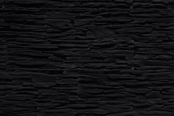 Black background. Wall faced with artificial stone imitating weathered slate. Colored in black. Monochrome photo.