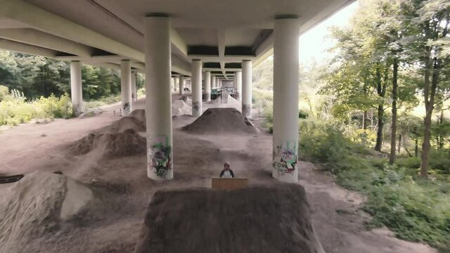 Drone shot  of mountainbiker on dirt jumper jumping over sand hill under highway bridge shot in 4k super slow motion