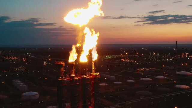 Flare stacks of the oil refinery are emitting fire at sunset