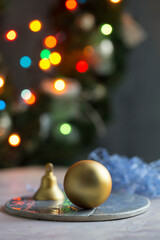  Christmas and New Year decoration with golden ball, bell on grey plate. Color lights on background. Close up