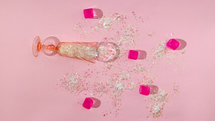 A pink Champagne glass with shiny tinsels on pink background. Fuchsia ice cubes and more tinsels...