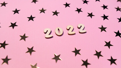 Cheerful wooden lettering happy new year 2022 on a soft gently pink background with gold stars. Sparkle confetti holiday concept 