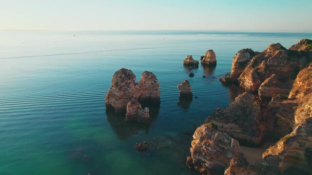 Aerial view of people Kayaking and Canoeing by Praia do Camilo, Lagos, Algarve. A scenic sunrise from above over the coastal rocky cliffs of Algarve with tourists having a relaxing luxury holiday.