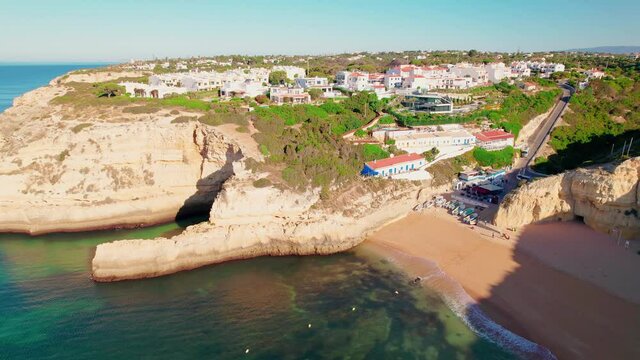 Aerial view of Benagil Beach, boats and vessels, hotels and restaurants in 4K. Benagil, Carvoeiro from above, a coastal tourist Village in Algarve popular of all the maritime caves in Portugal.