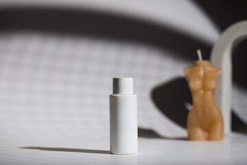 Plastic bottle of cosmetic product and decorative candle on table against shadows