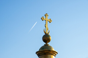 A golden Orthodox cross on a dome with a moon, an airplane flies across the blue sky. A sign. Orthodox church, temple .
