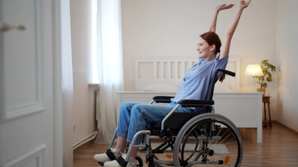 Obraz premium A young disabled woman is riding in her wheelchair around the room and stretching 