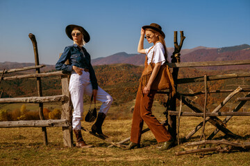 Outdoor full-length fashion portrait of two confident women wearing stylish outfits, posing in autumn mountains. Copy, empty space for text - 463931779