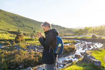 Side view young explorer man trekking in mountains, using mobile phone for GPS application....