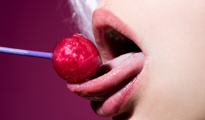 Lollipop in woman mouth, red lipstick. Woman licking a red shiny lollipop. Close up. Sexy woman with lollipop in sensual mouth. - obrazy, fototapety, plakaty