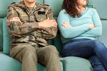 Cropped shot of a soldier and his unrecognizable wife sitting on the couch with their arms crossed...
