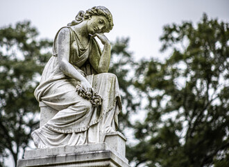 Fototapeta na wymiar worn statue of heavenly angel thinking in graveyard
