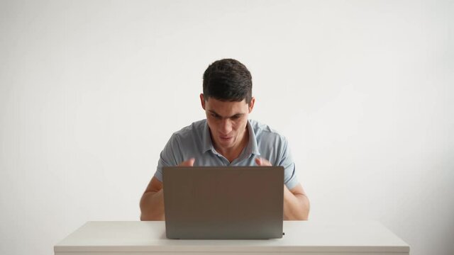 Happy office worker in in a blue polo shirt works on laptop and funny rejoices successful deal on white background. Emotions joy and happiness employee. Joy winning an online lottery or game