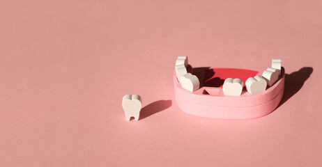 Wooden model of a human jaw with a missing tooth on a pink studio background. The problem of tooth...