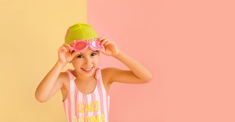 Funny joy girl in striped swimsuit and a Swimming Cap, puts on Swimming Goggles, isolated on an pink and yellow studio background. Learning to swim in the pool from an early age.  Happy baby