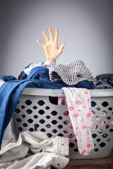 Abstract concept image with a woman's hand coming out of a basket full of clothes for laundry. She is overwhelmed and bored with housework and needs help. Repetitive never ending work