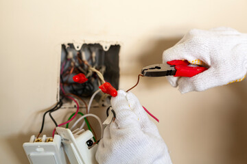 An electrician is replacing a wall switch. A DIY project concept. High voltage danger. rubber gloves are worn for protection. The professional is making a loop using pliers