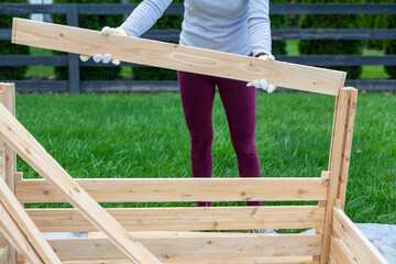 a woman is building a wooden fence or keep on tarp in her backyard. A concept for wood work. Furniture installation DIY project. She wears gloves to protect against wood splinters