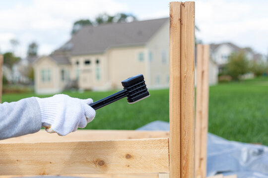 outdoor diy project in backyard with lawn. A person wearing safety gloves is installing a wooden fence or furniture using a plastic hammer to tighten. Concept image for worker, wood work.