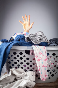 Abstract Concept Image With A Woman's Hand Coming Out Of A Basket Full Of Clothes For Laundry. She Is Overwhelmed And Bored With Housework And Needs Help. Repetitive Never Ending Work