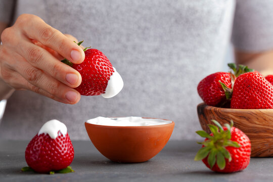 A caucasian woman is dipping a fresh ripe strawberry into cream or yoghurt. Concept image for healthy snack, indulge yourself, vegetarian diet and nutricious eating habits.