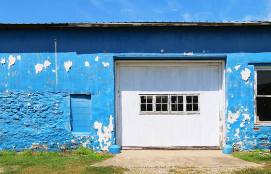 faded fading blue peeling painted stone block garage building with loading door and driveway