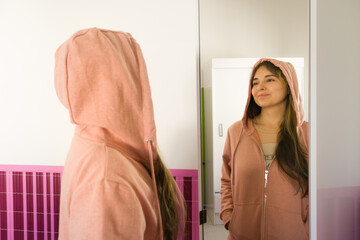 joven mujer morena feliz frente al espejo probándose o eligiendo ropa de abrigo con enfoque...