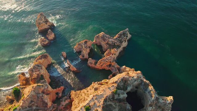 Drone 4K aerial view of sunset over Ponta da Piedade and Lagos town in Algarve. Best and most famous luxury holiday place in Portugal, rocky coastline seashores with turquoise ocean water and cliffs.