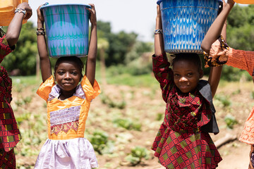 Closeup of two small black African girls carrying blue water buckets on their heads; child labour...