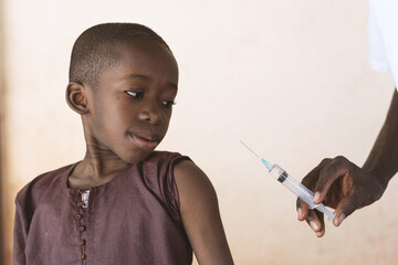 Healthcare professional holding a syringe with antimalarial vaccine to be injected to a small black...