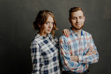 young couple in plaid shirts hugs on gray background