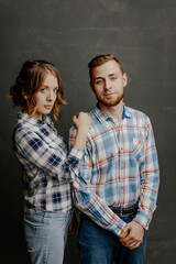 young couple in plaid shirts hugs on gray background