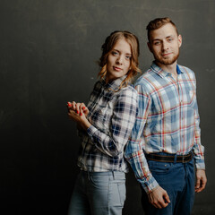 young couple in plaid shirts hugs on gray background