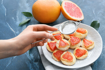 Woman sprinkling tasty grapefruit cookies with sugar powder on color background