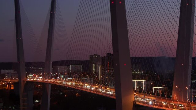 Great timelapse of the cable-stayed Golden Bridge across the Zolotoy Rog (Golden Horn Bay) and many busy cars driving along the road. The sky is turning dark. Sunset. Night cityscape