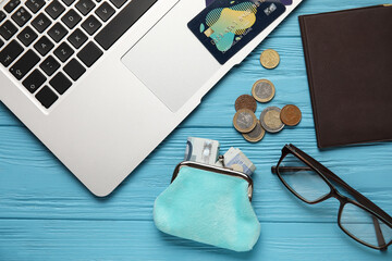 Wallet with money, eyeglasses, passport and laptop on blue wooden background