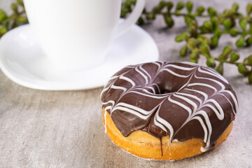 Closeup of delicious donut with icing on wooden background and white cup in composition