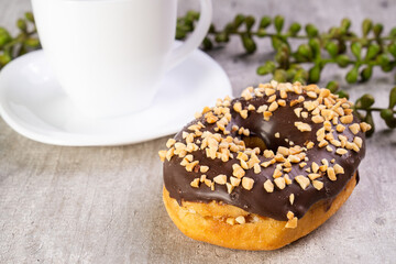 Closeup of delicious donut with icing on wooden background and white cup in composition