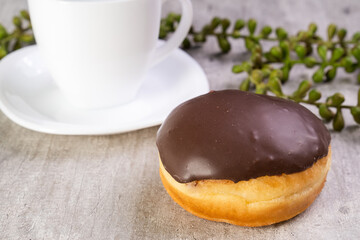 Closeup of delicious donut with icing on wooden background and white cup in composition
