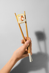Woman holding wooden chopsticks with delicious sushi roll on light background