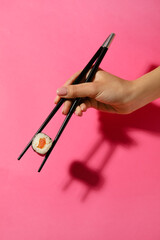 Woman holding chopsticks with salmon maki roll on color background © Pixel-Shot