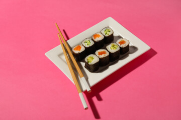 Plate with different maki rolls and wooden chopsticks on color background