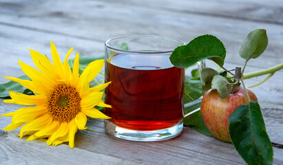Still life with a glass of tea, sunflower flowers and apples on a wooden background.