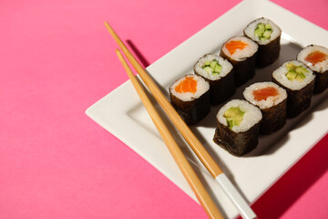 Plate with different maki rolls and wooden chopsticks on color background, closeup