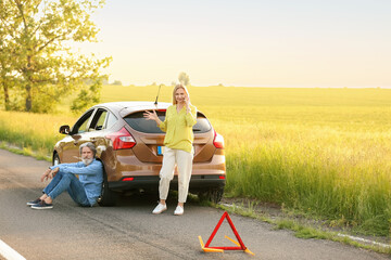 Stressed mature couple calling for help near damaged car outdoors