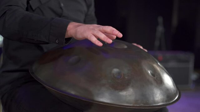 Close up view of musician hands playing handpan drum on big concert hall stage