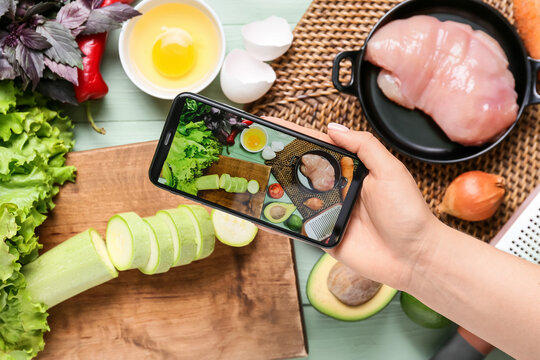 Woman holding mobile phone and taking picture of different ingredients on color wooden table