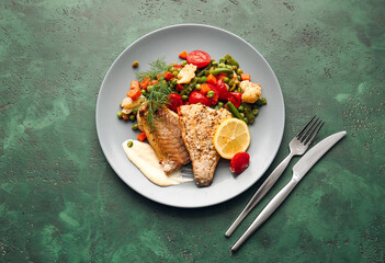 Plate with tasty baked cod fillet, vegetables and sauce on color background