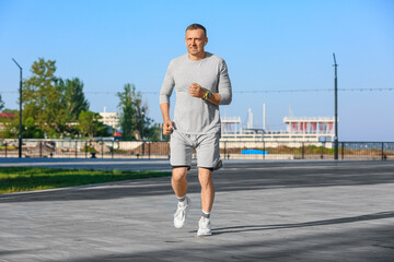 Fototapeta premium Sporty mature man in earphones running outdoors