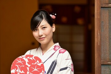 京都町屋の縁側でうちわ片手に微笑む浴衣姿の若い女性